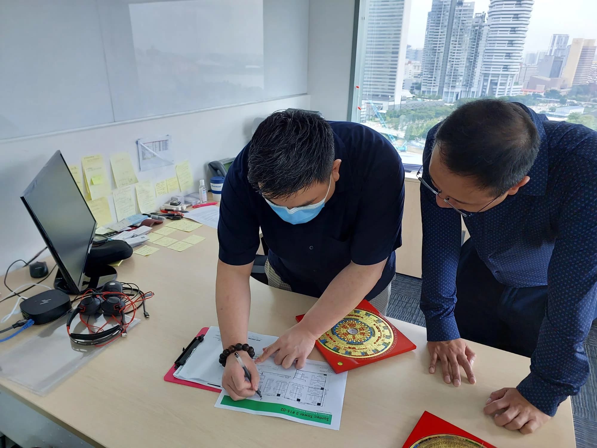 Master Alvin reviewing a floor plan on-site with a client, with a luopan compass on the desk